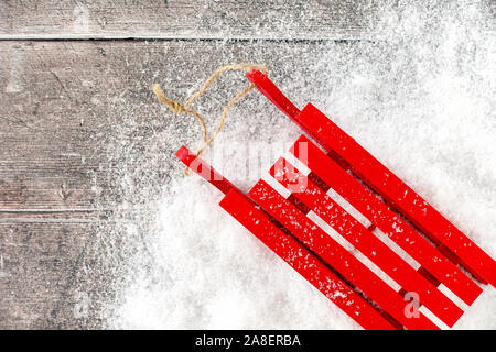 Rote Schlitten mit Schneeflocken im Schnee und auf Braun rustikale Holztafel Hintergrund mit Kopie Raum abgedeckt. Ansicht von oben. Stockfoto