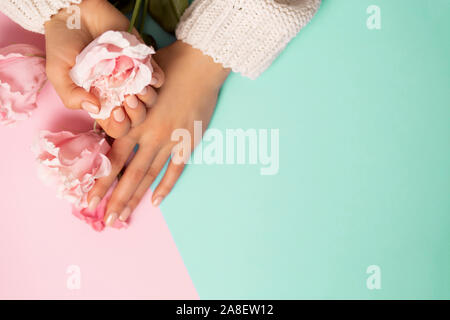 Pflege, Wellness, hochwertige, professionelle Maniküre, Beauty und Fashion Konzepte. Schöne rosa Pfingstrosen Rosen auf der Frau die Hände auf Minze und rosa Hintergrund, oben vi. Stockfoto