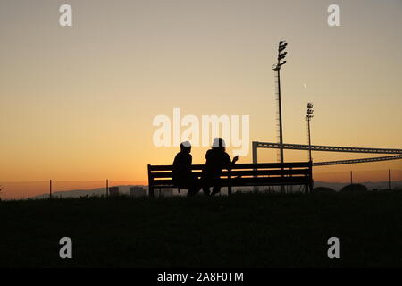 Ein Paar auf einer Bank sitzen im Sonnenuntergang am Rande der Stadt Barcelona Stockfoto