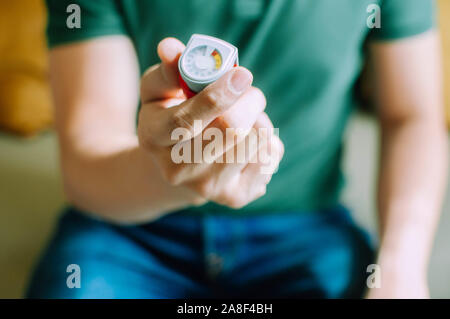 Ein junger Mann hält ein Asthma Inhalator gerät beim Sitzen auf einer Couch Stockfoto