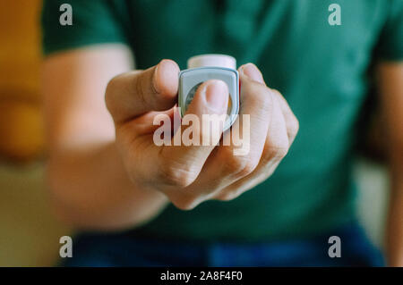 Ein junger Mann hält ein Asthma Inhalator gerät beim Sitzen auf einer Couch Stockfoto