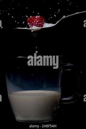 Erdbeere Spritzer auf einen Löffel voll Milch mit unter ein Glas mug teilweise gefüllt. Stockfoto