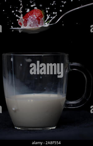 Erdbeere Spritzer auf einen Löffel voll Milch mit unter ein Glas mug teilweise gefüllt. Stockfoto