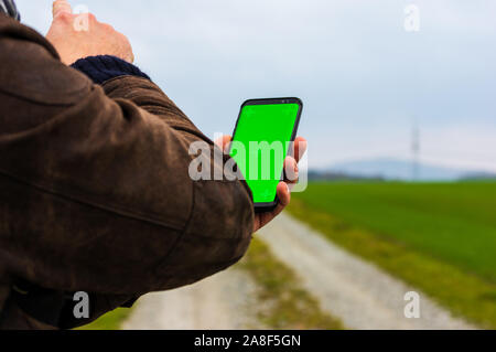 Wandern Mann mit leder jacke mit seinem Smart Phone in offenen Herbst Landschaft zu navigieren. Mit einem Handy Karte im Freien prüfen Stockfoto