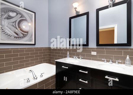 Eine blaue Badezimmer mit braunen Fliesen im Subway-Stil rund um das Bad, eine dunkel gefärbte Eitelkeit und ein Bild über den Rand der Badewanne. Stockfoto