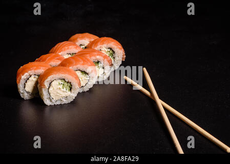 Verschiedene Arten von Sushi auf einem dunklen Hintergrund serviert. Rolle mit Lachs, Avocado, Gurke. Sushi Menü. Japanisches Essen. Stockfoto