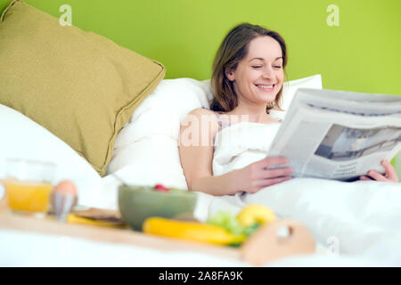 25 -30 jährige Frau schläft im Bett und liest die Zeitung, HERR: Ja Stockfoto