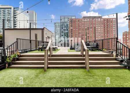 Eine Dachterrasse in Chicago mit Treppe führt zu einem Sitzbereich und einer Zeichenfolge lichter Overhead. Gebäude sind im Hintergrund mit einem blauen Himmel. Stockfoto