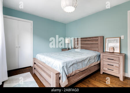 Ein kleines Schlafzimmer mit einem hellen Schlafzimmer möbel, türkisfarbenen Wänden, Holzböden und ein schickes Licht hängen. Stockfoto