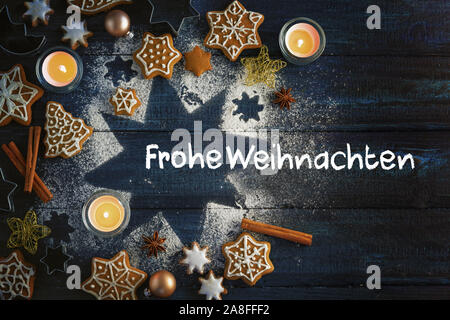 Gingerbread cookies, Gewürze und brennende Kerzen auf einem Stern aus Puderzucker auf einem dunkelblauen Hintergrund Holz, Deutsche text Frohe Weihnachten, d. h. Mich Stockfoto