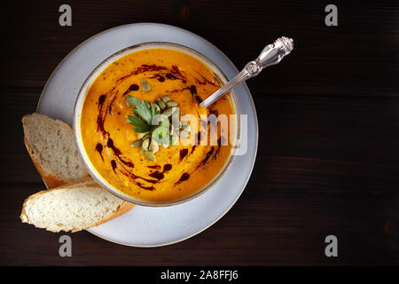 Kürbis Suppe pürieren, mit Samen, viel Grün und dunklen Kürbiskernöl in die weiße Schüssel auf einem schwarzen Hintergrund. Ansicht von oben. Stockfoto