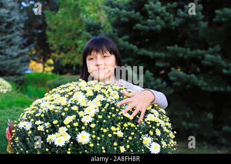 Ein nettes junges Mädchen von 11-14 Jahre alt Sitzt in der Nähe der Blumen und Blick in die Kamera. Porträt eines lächelnden Mädchen in einem Blatt. Gute Laune. Po Stockfoto