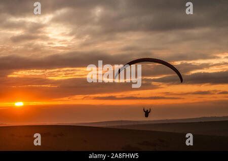 Devils Dyke, Brighton, East Sussex, Großbritannien..8. November 2019..Gleitschirmflieger, die auf der kalten Nordbrise gegen die untergehende Sonne & verstreute Wolken über den South Downs fliegen, machen atemberaubende Szenen aus. . Stockfoto