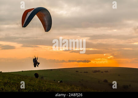 Devils Dyke, Brighton, East Sussex, Großbritannien..8. November 2019..Gleitschirmflieger, die auf der kalten Nordbrise gegen die untergehende Sonne & verstreute Wolken über den South Downs fliegen, machen atemberaubende Szenen aus. . Stockfoto