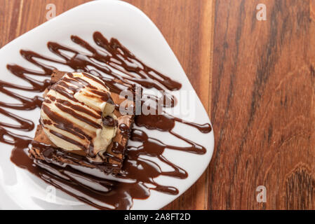 Chocolate Brownies mit Vanilleeis und chocolatel Sirup auf Holz- Hintergrund isoliert Stockfoto