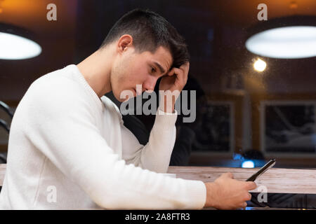Frustriert kaukasischen jungen Mann lesen Nachricht mit enttäuschenden Nachrichten auf digitale Smartphone. Stockfoto