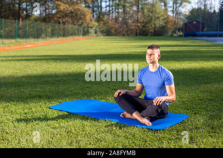 Junger Mann, der athletische Abnutzung im Park Training Yoga sitzen Stockfoto