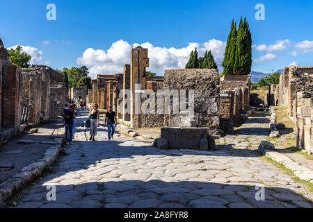 Touristen zu Fuß in eine gepflasterte Straße an der antiken Stadt Pompeji. Pompeji, Italien, Oktober 2019 Stockfoto