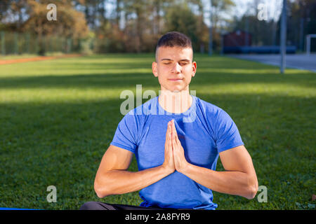 Junger Mann, der athletische Abnutzung im Park Training Yoga sitzen Stockfoto