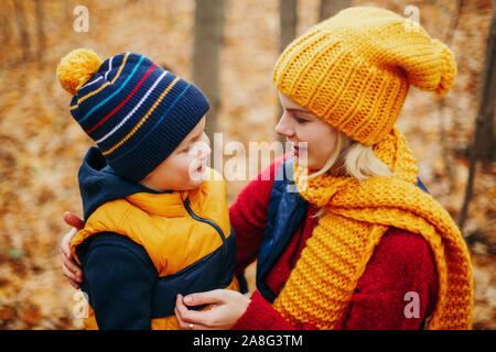 Kaukasische junge Mutter umarmt Gespräch mit cute adorable Toddler boy Sohn im Herbst park Outdoor mit gelb orange rot Baum Blätter. Glückliche Familie. Stockfoto