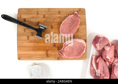 Rohes Schweinefleisch ohne Knochen Kotelett Koteletts und meat Tenderizer [auf einer hölzernen Schneidebrett, Nahaufnahme, direkt von oben, auf weißem Hintergrund Stockfoto