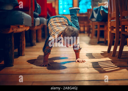 Cute adorable Junge drei Jahre alt Spaß im Cafe Restaurant. Kinder spielen auf dem Boden in der Öffentlichkeit. Freiheit der Meinungsäußerung und Verhalten für Stockfoto