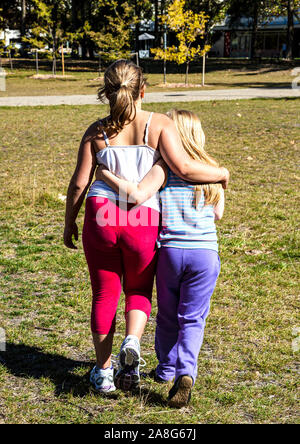 Junge weibliche Cousins zu Fuß entfernt von der Kamera mit Arme um einander in lokalen Park Stockfoto