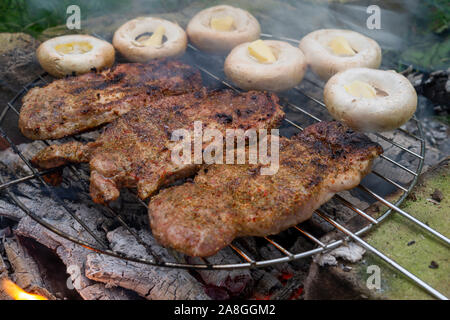 Drei Portionen Fleisch und Pilze mit Farbtupfer butter Grillen auf einem Grill Feuer über Holz Kohlen in der Nähe zu sehen. Stockfoto