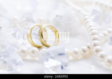 Zwei goldene Ringe mit Perlenkette und auf weißem Hintergrund als Symbol der Liebe und der Verbindung Stockfoto