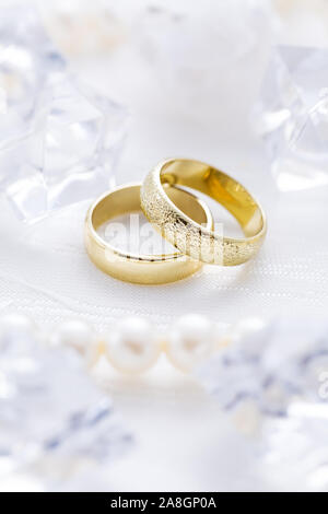 Zwei goldene Ringe mit Perlenkette und auf weißem Hintergrund als Symbol der Liebe und der Verbindung Stockfoto
