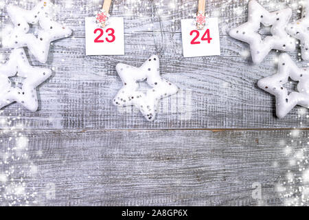 23-24 Teil der Adventskalender mit Blätter mit Zahlen auf dekorative Clips und weiße Weihnachten Spielzeug Sterne auf weißem Holz- snowy Hintergrund mit Kopieren s Stockfoto