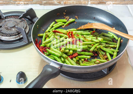 Französische grüne Bohnen, getrocknete Chilis und Knoblauch unter Rühren braten Topf auf Herd. Home Küche essen. Stockfoto