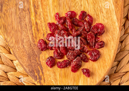 Getrocknete Cranberries auf einer Mango Holz Brett, einen gesunden Snack, in natürlichem Licht, front Fokus zu rücken, von oben. Stockfoto