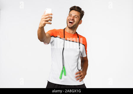 Stattlich, männlichen Athleten nehmen selfie nach dem Training im Fitnessraum, halten Smartphones mit verlängerter Arm und lächelt zufrieden und stolz, dass Anhänger neue Stockfoto