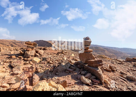 Blick auf die bunten Berge und das Tal von Eilat Red Canyon mit Cairns im Vordergrund gegen den blauen Himmel mit Wolken. Israel Stockfoto