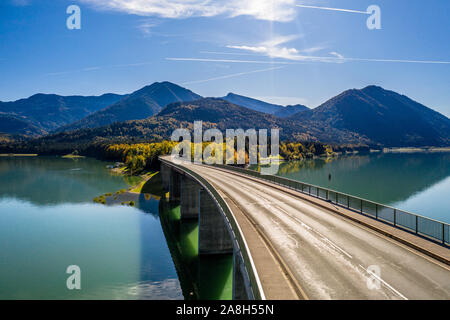 Malerische Luftaufnahme der Brücke über den See Sylvenstein mit schönen Reflexionen. Alpen Karwendelgebirge im Rücken. Herbst Landschaft von Bayern Stockfoto