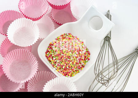 Stapel von dekorativen Zucker Sterne in einer Schüssel mit einem Schneebesen sticks für Eier und weiß und rosa Papier Formen für Muffins Stockfoto