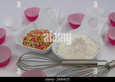 Weißes Mehl und gefärbter Zucker Sterne in zwei weiße Schalen, treibend Stangen und Papier Grundlagen für Muffins auf weißem Hintergrund Stockfoto