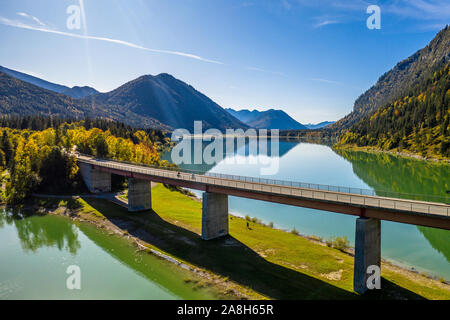 Malerische Luftaufnahme der Brücke über den See Sylvenstein mit schönen Reflexionen. Alpen Karwendelgebirge im Rücken. Herbst Landschaft von Bayern Stockfoto