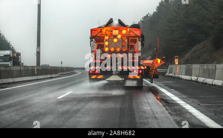 Orange highway maintenance Streuer Lkw Verbreitung Auftausalz, kristalle fallen auf dem Eis bedeckt Asphaltstraße bei bewölkter Tag Stockfoto