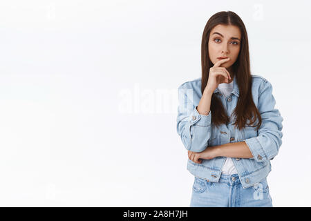 Skeptisch, misstrauisch - nachdenklich kaukasische Mädchen in Jeans Jacke suchen, berühren die Lippe und heben eine Augenbraue verdächtig, Zweifel haben, vermuten Stockfoto