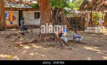 Malindi, Kenia - April 06, 2015: Unbekannter lokaler Kinder sitzen auf Tree root vor ihrem Haus. Die Lebensbedingungen in diesem Bereich sind in der Regel schlecht. Stockfoto