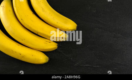 Von oben nach unten anzeigen, vier Bananen auf schwarzem Schiefer, Platz für Text auf der rechten Seite. Stockfoto