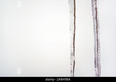 Zwei Eiszapfen hängen von Dach, weiß bedeckt Hintergrund, Platz für Text auf der linken Seite. Stockfoto