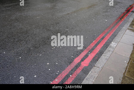 Doppelte rote Linie in der Nähe der Bordsteinkante auf nassem Asphalt. In London diese zeigen stoppen jederzeit verboten, und statt der gelben Linien manchmal verwendet. Stockfoto