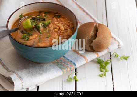 Herzhafte vegane Suppe mit braunen Reis, Okra und Spinat in einer Schüssel auf einem weißen Tisch serviert. Stockfoto
