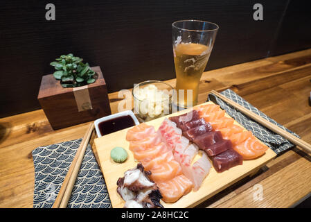 Eine Nahaufnahme von einem leckeren Teller mit frischem Sashimi in einer Sushi Bar mit Bier und Sojasauce und Ingwer