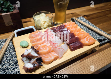 Eine Nahaufnahme von einem leckeren Teller mit frischem Sashimi in einer Sushi Bar mit Bier und Sojasauce und Ingwer