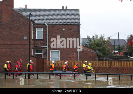 Feuerwehr und Rettungsdienste evakuieren ein behinderter Mann aus seinem Haus nach dem Hochwasser im Bentley Bereich von Doncaster nach einem Monate Niederschlag fielen auf einen Tag caausing den Don seine Banken zu verletzen. Stockfoto