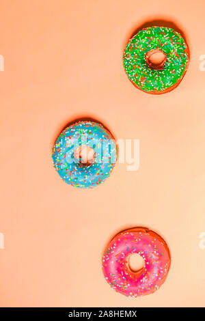 Nahaufnahme von drei bunten pink, blau und grün glasierten süßen Donuts auf farbigen Hintergrund, Ansicht von oben. Essen, Restaurant, Bäckerei Konzept Stockfoto